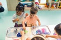 Sensory play at multi-cultural nursery school. Toddlers with their teacher playing with striped straws and milk painting Royalty Free Stock Photo