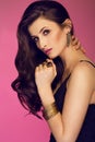 Sensual beautiful brunette woman posing in black dress and gold jewlery looking at the camera. Girl with long curly hair. Royalty Free Stock Photo