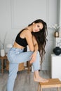 Sensual beautiful young Caucasian woman with long hair in a black top and jeans posing for the camera in the living room Royalty Free Stock Photo