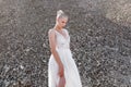 Beautiful blonde female model in a white wedding dress, posed behind piles of stones during the day Royalty Free Stock Photo