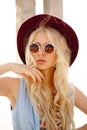 Stylish girl poses on the sunshine place, wearing in a hat and round floral sunglasses, touching sensual her face. Royalty Free Stock Photo