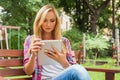 Sensual blonde woman sitting in park on wooden bench. She is using tablet pc. Outdoor photo. She looks relaxed. Royalty Free Stock Photo