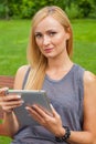 Sensual blonde woman sitting on wooden bench in park. She is using white tablet pc. Outdoor photo. She looks relaxed. Royalty Free Stock Photo