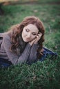 Sensual brunette lady with pout pink lips and white cheeks wearing casual cosy sweater with fur posing sit for on green grass in a Royalty Free Stock Photo