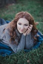 Sensual brunette lady with pout pink lips and white cheeks wearing casual cosy sweater with fur posing sit for on green grass in a Royalty Free Stock Photo