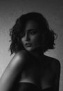 Sensual brunette model with curly hair and naked shoulders posing with contrast light, Black and white photo