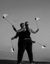 Sensual couple of fire performers perform dance with flaming poi on blue sky outdoors, desire