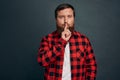 Sensual and dreamy handsome bearded man in red checkered shirt, shushing and squinting passionatly, keep secret, asking be quiet,