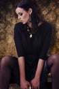 Sensual fashion model in black clothes with jewellery over golden pattern background Royalty Free Stock Photo