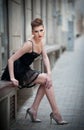 Sensual girl with long legs, short black dress and high heels sitting on the bench.Handsome girl wearing short skirt and high heel