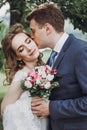 Sensual groom kissing beautiful bride on the cheek, newlywed couple portrait, beautiful married couple posing outdoors