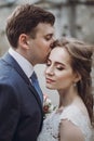 Sensual groom kissing beautiful bride on the forehead, newlywed couple portrait, beautiful married couple posing outdoors