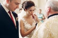 Sensual happy groom kissing wedding ring during wedding ceremony in christian catholic church, priest holding wedding ring in