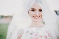 Sensual portrait of beautiful happy bride smiling under veil holding bouquet outdoors. Gorgeous bride in white gown with modern Royalty Free Stock Photo