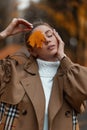 Sensual portrait of a beautiful pretty young woman in stylish warm clothes with a maple yellow leaf near face.Attractive cute girl Royalty Free Stock Photo