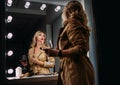 Sensual portrait of middle-aged seductive woman with red wine glass gazing at mirror reflection appreciating her Trench coat Royalty Free Stock Photo