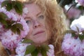 Sensual portrait of a sexy, soulful, pensive, mature redhead woman, best age, behind pink flower tree blossoms, spring awakening,