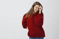 Sensual and romantic woman in red loose warm sweater flirting, posing tender and cute smiling shy looking down, touching