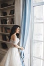 Sensual and seductive brunette model girl in stylish lace dress with naked shoulders looks through the window and posing near book Royalty Free Stock Photo