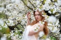 Sensual, seductive, innocent portrait of a sexy, young redhead woman in white dress in white flower tree blossoms, spring