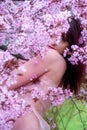 Sensual, seductive, portrait of a sexy, young, brunette woman in pink dress in pink flower tree blossoms in spring awakening,