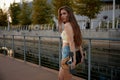 Sensual slim young woman walking with longboard over summer cityscape