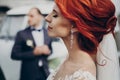 Sensual stylish bride holding modern bouquet and relaxing with windy hair and groom looking at her near retro car. luxury wedding Royalty Free Stock Photo