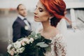 Sensual stylish bride holding modern bouquet and relaxing with windy hair and groom looking at her near retro car. luxury wedding Royalty Free Stock Photo