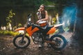 Charming tattooed racer girl wearing motocross outfit with semi naked torso leaning on her bike and looking on camera in