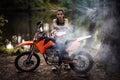 Charming tattooed racer girl wearing motocross outfit with semi naked torso leaning on her bike and looking on camera in
