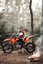 Charming young female racer wearing motocross outfit with semi naked torso leaning on her bike and looking on a camera