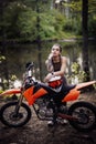 Charming tattooed racer girl wearing motocross outfit with semi naked torso leaning on her bike and looking on camera in