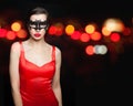 Sensual woman in black carnival mask wearing red silky dress on abstract night glitter bokeh background Royalty Free Stock Photo