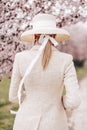 Sensual woman with blond hair in elegant dress and accessories posing among blossoming peach trees in park Royalty Free Stock Photo