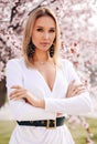 Sensual woman with blond hair in elegant dress and accessories posing among blossoming peach trees in park Royalty Free Stock Photo