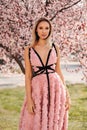 Sensual woman with blond hair in elegant dress and accessories posing among blossoming peach trees in park Royalty Free Stock Photo