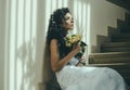Sensual woman with wedding bouquet. Woman with flowers sit on staircase. Girl with bridal makeup and hairstyle. Bride in