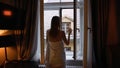 Sensual woman in white bedsheet walking and looking out of window