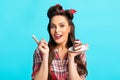 Sensual young pinup lady in retro outfit eating delicious cake, having cream on her finger, blue studio background Royalty Free Stock Photo