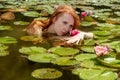 Sensual young redhead woman mermaid swims plays sensitively seductive with pink water lilies in the water Royalty Free Stock Photo