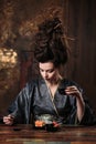 Sensual young woman in a geisha asian costume with fashion makeup and hair style drinks tea and eats sushi