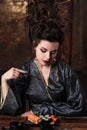 Sensual young woman in a geisha asian costume with fashion makeup and hair style eats sushi