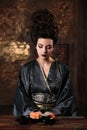 Sensual young woman in a geisha asian costume with fashion makeup and hair style eats sushi