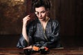 Sensual young woman in a geisha asian costume with fashion makeup and hair style eats sushi