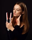 Sensual young woman with silky straight hair stands with eyes closed holding white modern hair straightener in hand Royalty Free Stock Photo