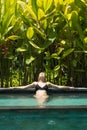 Sensual young woman relaxing in outdoor spa infinity swimming pool surrounded with lush tropical greenery of Ubud, Bali.