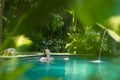 Sensual young woman relaxing in outdoor spa infinity swimming pool surrounded with lush tropical greenery of Ubud, Bali.