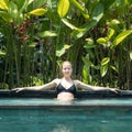 Sensual young woman relaxing in outdoor spa infinity swimming pool surrounded with lush tropical greenery of Ubud, Bali.