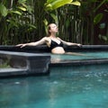 Sensual young woman relaxing in outdoor spa infinity swimming pool surrounded with lush tropical greenery of Ubud, Bali.