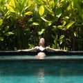 Sensual young woman relaxing in outdoor spa infinity swimming pool surrounded with lush tropical greenery of Ubud, Bali.